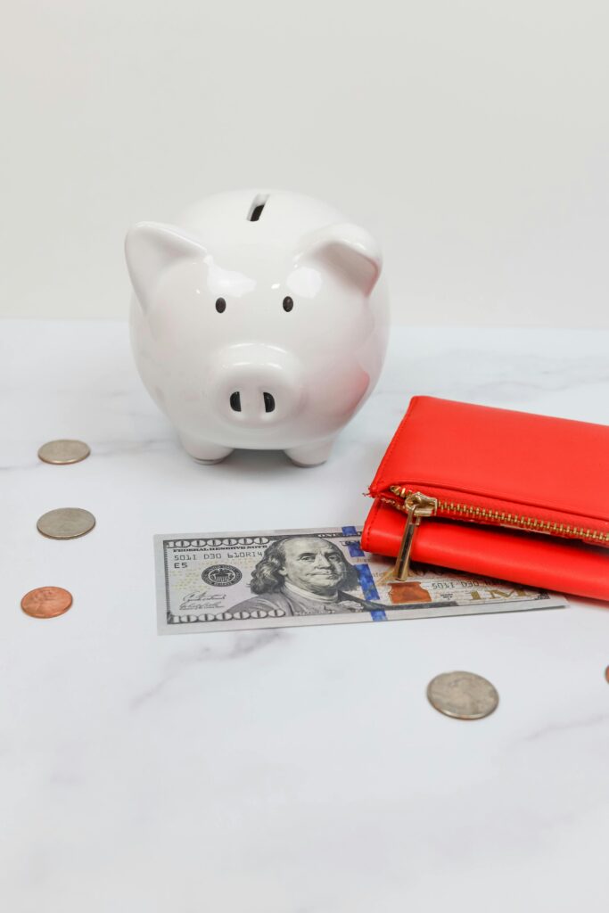White piggy bank with coins and a red wallet on a marble desk.