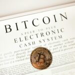 Bitcoin cryptocurrency coin on top of its white paper. Digital currency concept.