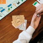 Hands holding dice near Monopoly board with fake money on table.