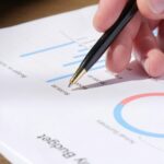 Close-up of hand analyzing data on a monthly budget document with graphs and charts.
